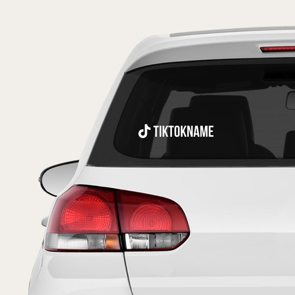 A white car rear window with a white TikTok name decal applied to the glass, shown against a light gray studio background.
